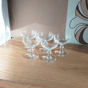 Peut inclure: Six coupes à champagne en verre transparent avec un design délicat. Les verres sont disposés en groupe sur une surface en bois.