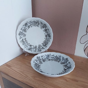 Puede incluir: Dos cuencos de cerámica blanca con diseños florales negros. Los cuencos tienen un borde festoneado y un borde elevado.