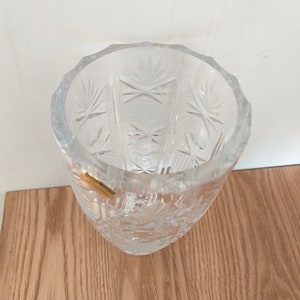 May include: A clear glass vase with a cut glass design. The vase is empty and has a gold sticker on the side.