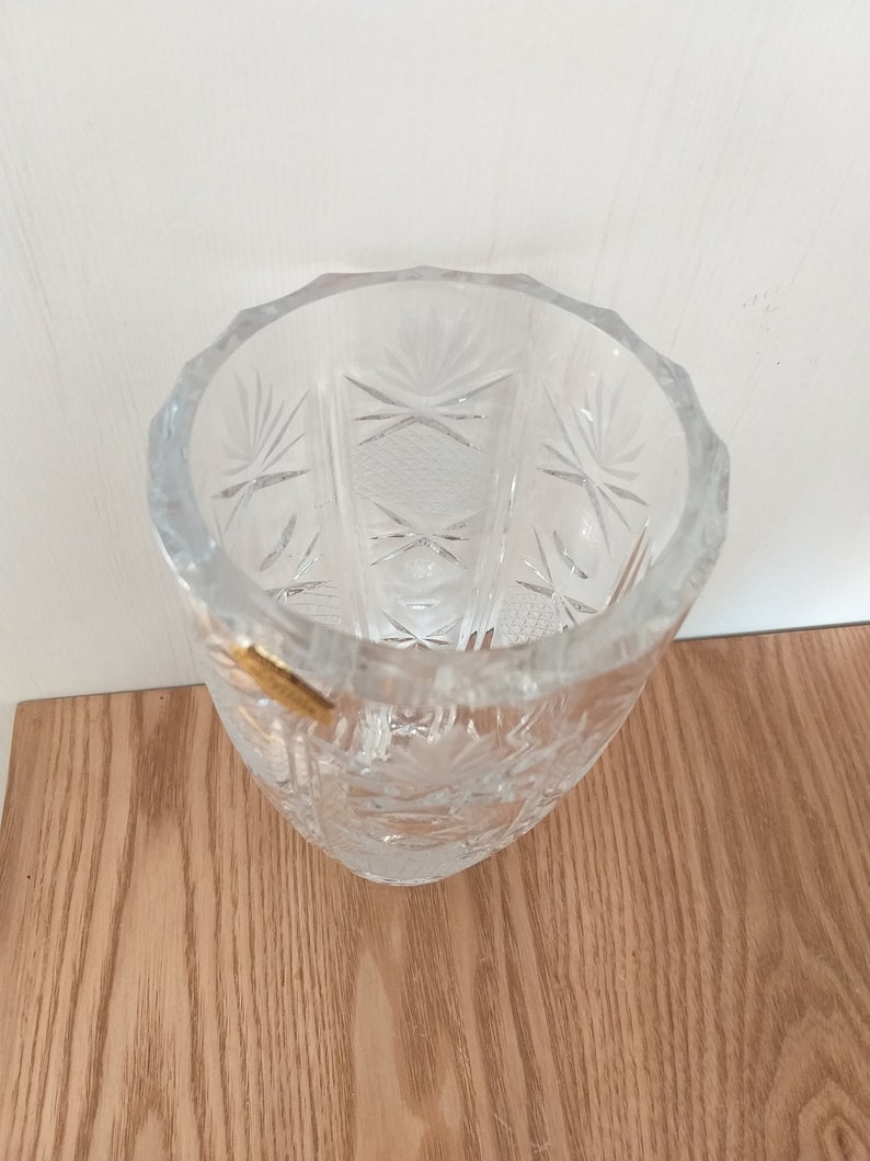 May include: A clear glass vase with a cut glass design. The vase is empty and has a gold sticker on the side.