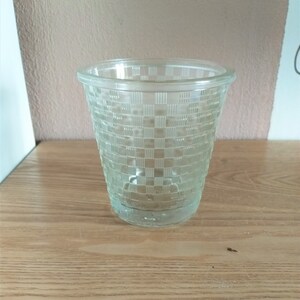 Op de afbeelding: Een helder glazen beker met een geruit patroon. De beker is leeg en staat op een houten oppervlak.