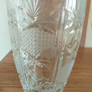 May include: A clear glass vase with a cut crystal design. The vase has a label that reads "Cristal Au-Ploy".