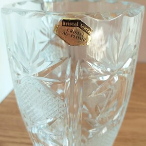 May include: A clear glass vase with a cut crystal design. The vase has a label that reads "Kristal Sajica Cristal Au-Plomb".