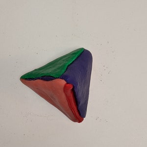 May include: A triangular shaped object made of three different colors of play dough. The top of the triangle is green, the left side is purple, and the right side is red.