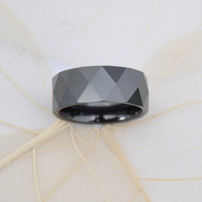 May include: A black tungsten carbide ring with a faceted design.