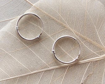 May include: Two silver hoop earrings on a light brown textured background.