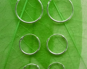 May include: Five silver hoop earrings of different sizes on a green leaf background.
