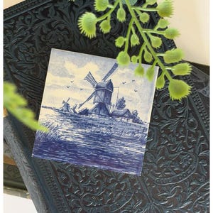 May include: A white ceramic mug with a black handle and the text "But First, Coffee" in a bold, black font. The mug is set against a blurred background, suggesting a cozy setting.