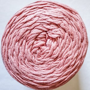 May include: A tightly wound ball of dusty rose yarn. The yarn is arranged in concentric circles, creating a spiral pattern. The texture of the yarn appears soft and slightly fuzzy, suggesting a natural fiber. Ideal for knitting or crocheting projects.