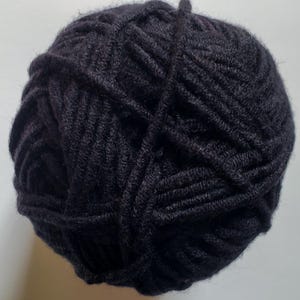May include: A ball of dark charcoal yarn, tightly wound. The yarn appears to be a thick, textured fiber, suitable for knitting or crocheting projects. The ball is round and compact, with visible strands.