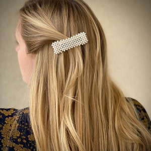 Könnte beinhalten: Eine rechteckige Haarklammer aus weißen Perlen. Die Klammer befindet sich im Haar einer Frau.
