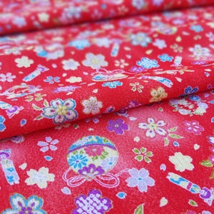 May include: Red fabric with a repeating pattern of small white flowers, blue and green leaves, and colorful ornaments with gold accents.