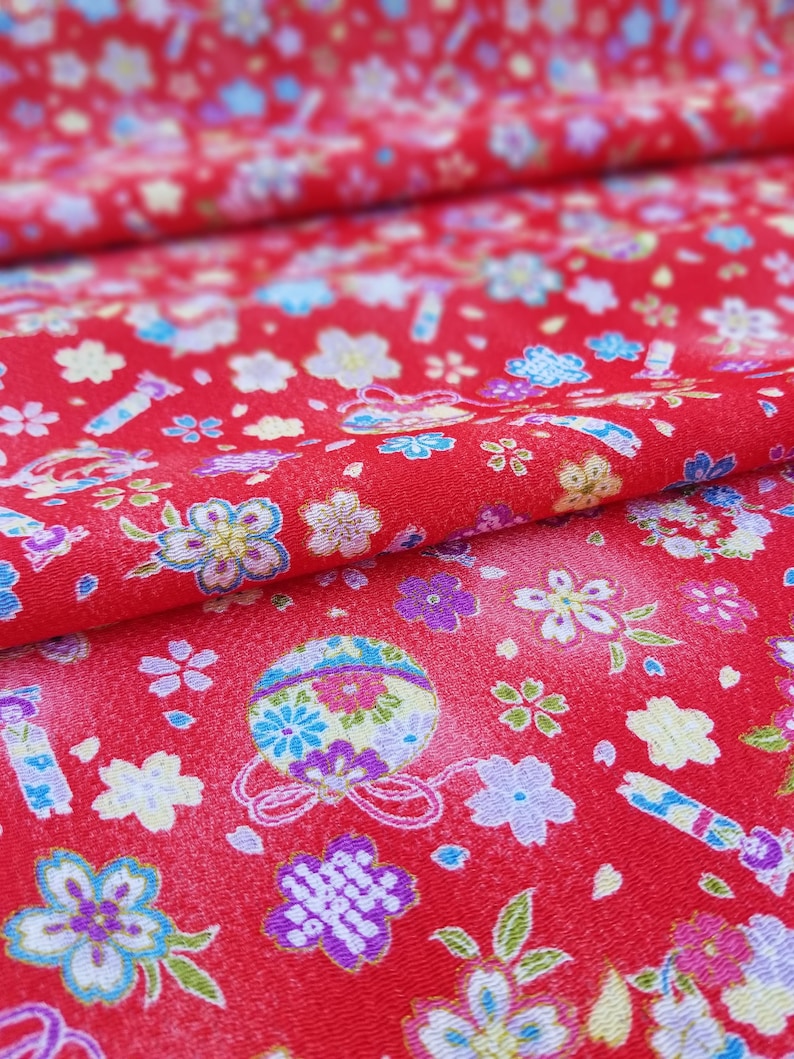 May include: Red fabric with a repeating pattern of small white flowers, blue and green leaves, and colorful ornaments with gold accents.