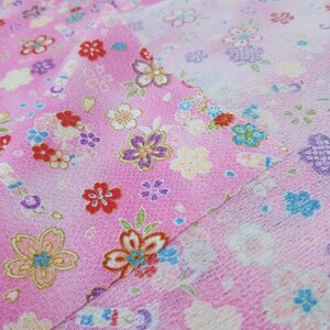 May include: Pink fabric with a floral pattern. The fabric features a variety of pink, white, blue, and yellow flowers. The fabric is folded in half, showing the pattern on both sides.