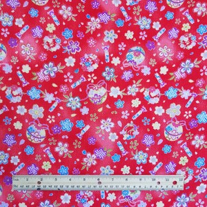 May include: Red fabric with a repeating pattern of small white, blue, and pink flowers, gold and silver ornaments, and red and gold sticks. The fabric is measured with a ruler in inches.