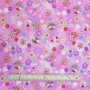 May include: Pink fabric with a repeating pattern of small flowers, ornaments, and candy canes. The fabric is 12 inches wide.