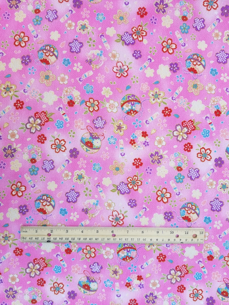 May include: Pink fabric with a repeating pattern of small flowers, ornaments, and candy canes. The fabric is 12 inches wide.