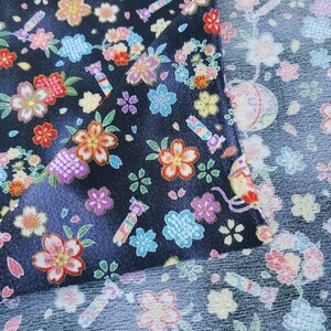 May include: Black fabric with a repeating pattern of colorful flowers and candy. The fabric is shown folded over, revealing a similar pattern on the back side.