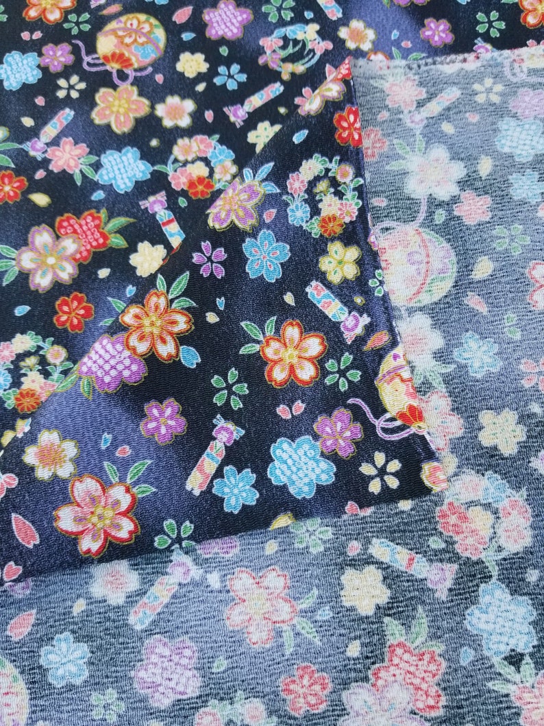 May include: Black fabric with a repeating pattern of colorful flowers and candy. The fabric is shown folded over, revealing a similar pattern on the back side.