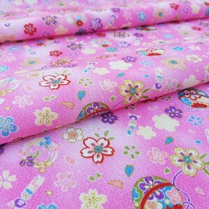 May include: Pink fabric with a repeating pattern of small flowers and a larger, colorful, round design. The fabric has a subtle ombre effect, fading from a darker pink to a lighter pink.