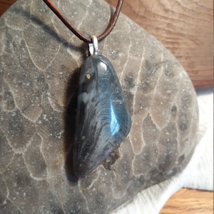 Könnte beinhalten: Ein dunkelgrauer und blauer Steinanhänger mit goldenen Flecken, der an einem braunen Lederband hängt.
