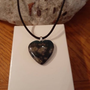 Könnte beinhalten: Eine Halskette mit einem herzförmigen Anhänger aus einem schwarz-weiß gesprenkelten Stein an einem schwarzen Lederband.