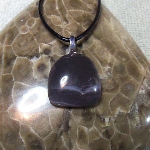 Könnte beinhalten: Ein dunkelgrauer Achat-Anhänger mit einem weißen Band, der an einem schwarzen Lederband hängt.