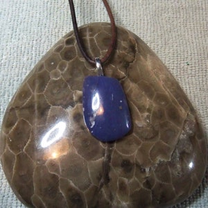 Könnte beinhalten: Ein blauer Edelstein-Anhänger an einer braunen Lederkordel. Der Anhänger ist oval geformt und hat eine silberne Öse.