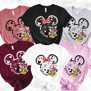 Puede incluir: Una colecci&oacute;n de seis camisetas en varios colores, incluyendo negro, blanco, rosa y burdeos. Cada camiseta presenta un dise&ntilde;o de Minnie Mouse con un lazo rojo, estrellas y personajes de Disney. La palabra "Disney" est&aacute; impresa debajo.