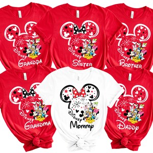 Puede incluir: Camisetas rojas y blancas con dise&ntilde;os de personajes de Disney. Las camisetas presentan orejas de Mickey Mouse, fuegos artificiales y las palabras "Grandpa", "Sister", "Brother", "Grandma", "Mommy" y "Daddy".