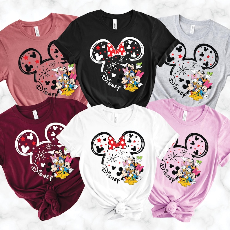 Puede incluir: Una colecci&oacute;n de seis camisetas en varios colores, incluyendo negro, blanco, rosa y burdeos. Cada camiseta presenta un dise&ntilde;o de Minnie Mouse con un lazo rojo, estrellas y personajes de Disney. La palabra "Disney" est&aacute; impresa debajo.