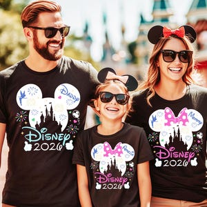 May include: Three people wearing black t-shirts with Disney designs. The shirts feature a Mickey Mouse head silhouette with a castle, fireworks, and the text "Disney 2026". The shirts also have the words "Daddy", "Mommy", and "Amelia".