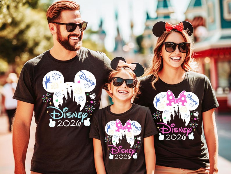 May include: Three people wearing black t-shirts with Disney designs. The shirts feature a Mickey Mouse head silhouette with a castle, fireworks, and the text "Disney 2026". The shirts also have the words "Daddy", "Mommy", and "Amelia".