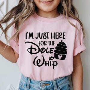 May include: Pale pink t-shirt featuring the text "I'M JUST HERE FOR THE Dole Whip" in black. The design includes a black Dole Whip soft serve ice cream cone with a Mickey Mouse head silhouette. The shirt is worn by a child.