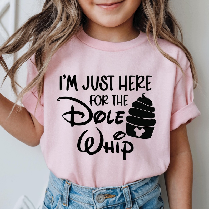 May include: Pale pink t-shirt featuring the text "I'M JUST HERE FOR THE Dole Whip" in black. The design includes a black Dole Whip soft serve ice cream cone with a Mickey Mouse head silhouette. The shirt is worn by a child.