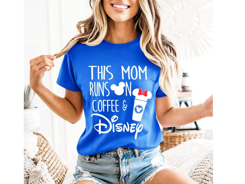 May include: Royal blue t-shirt with white text that reads "THIS MOM RUNS ON COFFEE & Disney." The design includes a coffee cup with a red bow and a Mickey Mouse head. The shirt is a crew neck.