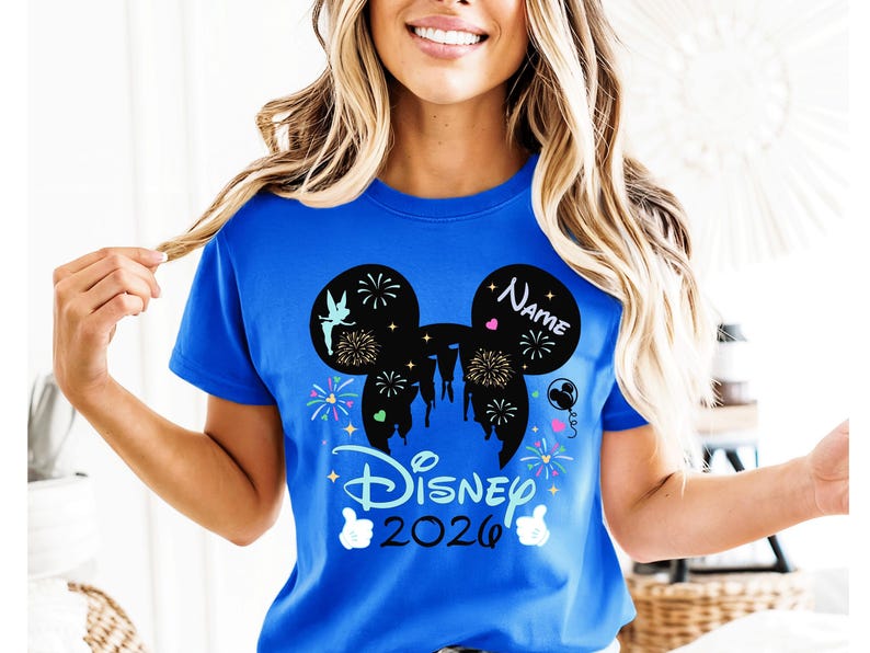 May include: A royal blue t-shirt with a black Mickey Mouse silhouette design, including fireworks, a castle, and a fairy. The shirt displays "Disney 2026" and a space for a name. White gloves are at the bottom of the design.
