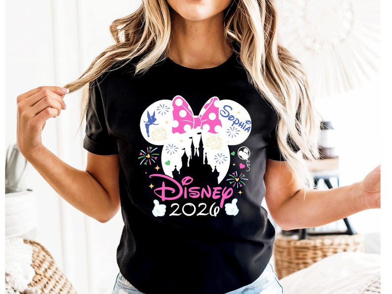 May include: Black t-shirt with a Disney-themed design. It features a pink polka-dot bow, a castle silhouette, and the text "Disney 2026". The design includes fireworks and the name "Sophia" in a Disney font.