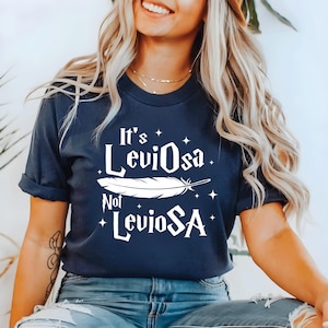 May include: Navy blue t-shirt with the text "It's Leviosa, Not LevioSA" in white, along with a feather graphic and stars. The shirt is a casual style.