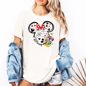 Puede incluir: Camiseta color crema con un contorno negro de las orejas de Mickey Mouse, un lazo rojo y estrellas. La camiseta tiene un gr&aacute;fico de Disney con Mickey, Minnie, Donald, Daisy y Goofy. La modelo lleva una chaqueta vaquera.