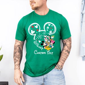 Puede incluir: Una camiseta verde con un dise&ntilde;o de Mickey Mouse y el texto "Disney Custom Text". El dise&ntilde;o incluye orejas de Mickey Mouse con detalles rojos y blancos, y un grupo de personajes de Disney.