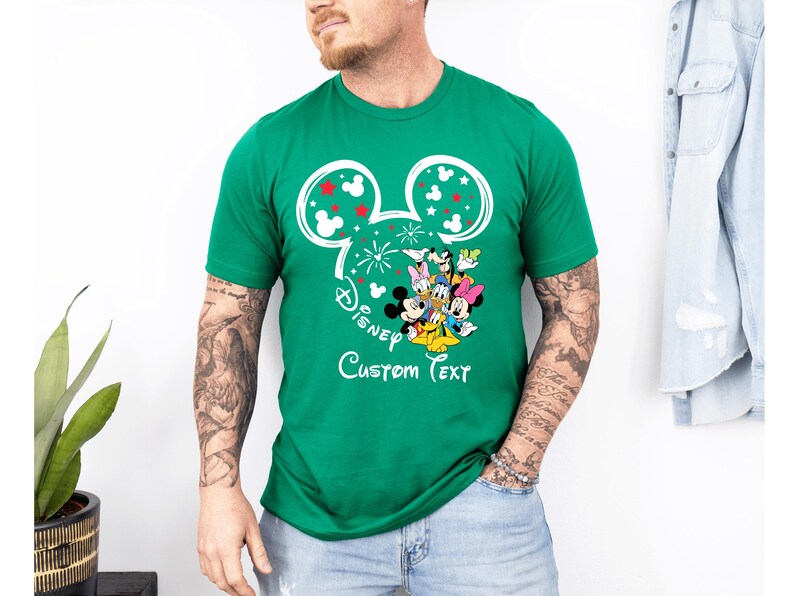 Puede incluir: Una camiseta verde con un dise&ntilde;o de Mickey Mouse y el texto "Disney Custom Text". El dise&ntilde;o incluye orejas de Mickey Mouse con detalles rojos y blancos, y un grupo de personajes de Disney.