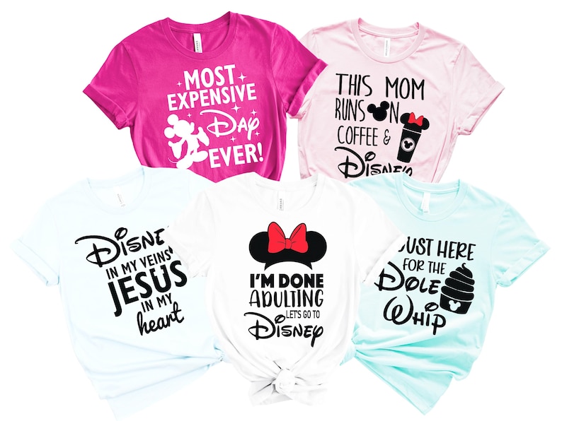 May include: Five colourful t-shirts with Disney-themed text. The shirts are pink, light pink, white, and light blue. Text includes "Most Expensive Day Ever!", "This Mom Runs on Coffee & Disney", "Disney in my veins Jesus in my heart", "I'm done adulting lets go to Disney", and "Just here for the Dole Whip".