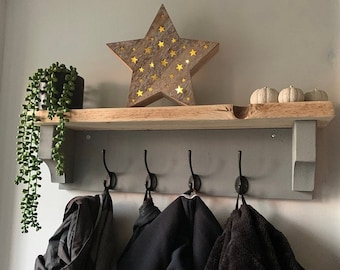 May include: A gray wooden coat rack with four black hooks, a shelf, and a decorative star with star-shaped cutouts. The shelf holds a small potted plant and three small white pumpkins. Coats and jackets hang from the hooks.