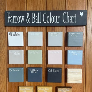 May include: A wooden color chart displaying various paint colors from Farrow & Ball. The chart includes color samples like "All White," "Ammonite," "Pavillion Grey," and "Plummet Grey." The sign above reads "Farrow & Ball Colour Chart."