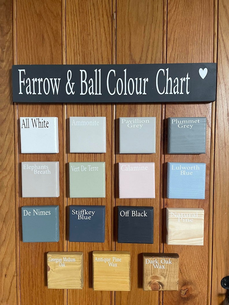 May include: A wooden color chart displaying various paint colors from Farrow & Ball. The chart includes color samples like "All White," "Ammonite," "Pavillion Grey," and "Plummet Grey." The sign above reads "Farrow & Ball Colour Chart."