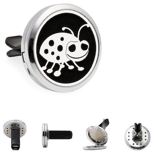 May include: Silver car air freshener with a black and white ladybug design. The air freshener has a clip to attach to a car vent.