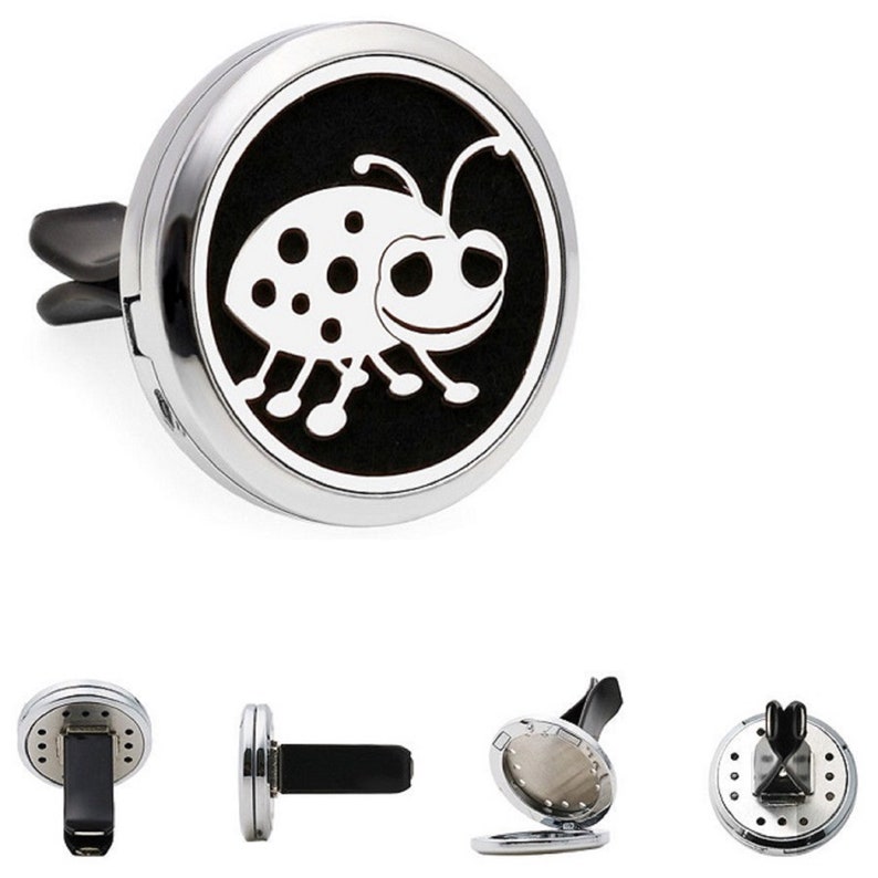 May include: Silver car air freshener with a black and white ladybug design. The air freshener has a clip to attach to a car vent.