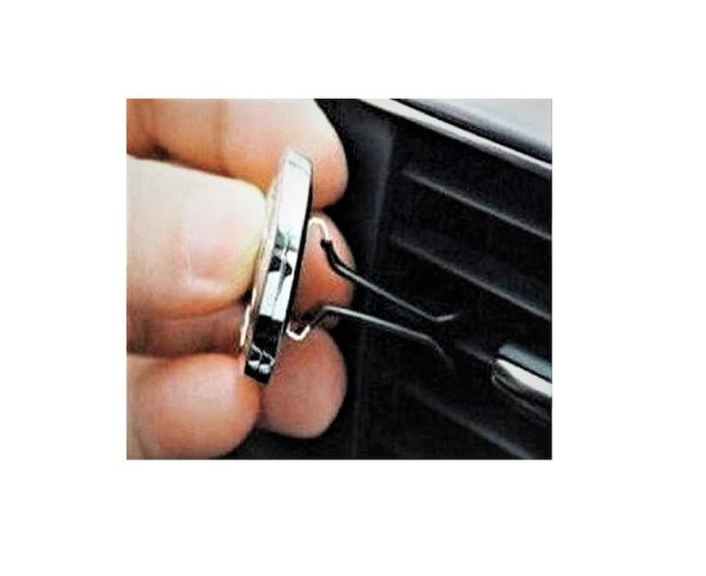 May include: A silver car air freshener with a black clip. The clip is attached to a car air vent.