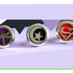 May include: Five silver car air freshener medallions with different designs. The designs include a dragonfly, a crescent moon with a star, a Superman logo, a butterfly, and a pair of angel wings.